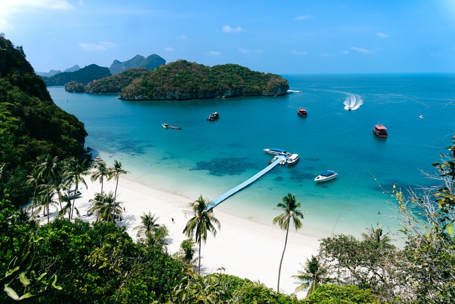 Stunning aerial view of a tropical beach with boats and lush islands under a clear sky.