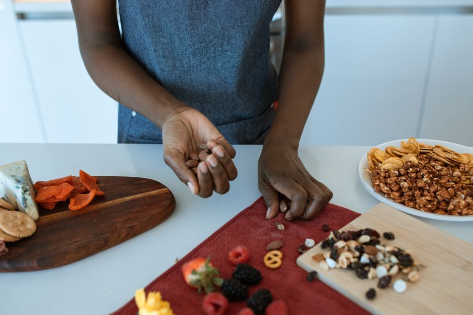 A detailed view of a person preparing a charcuterie board with a variety of snacks and fruits.
