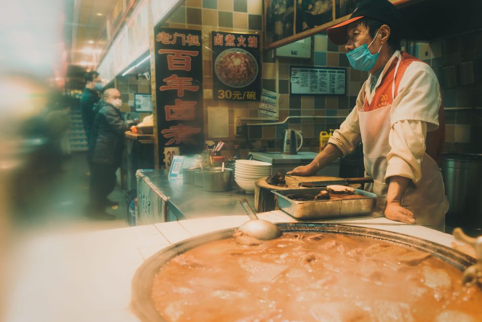 A street vendor prepares a traditional Chinese hotpot in a vibrant indoor market setting.