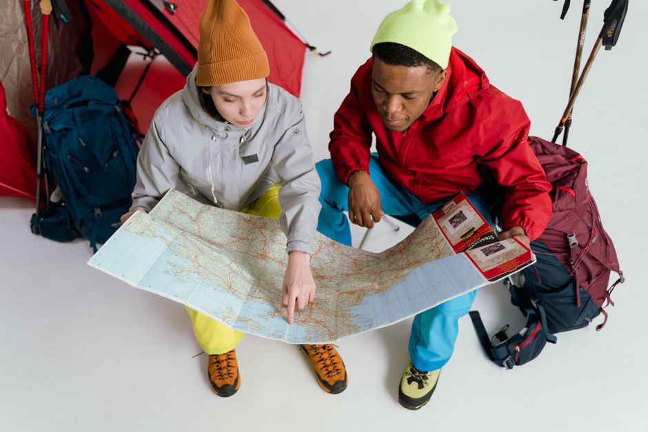 Two young adventurers studying a map in a studio setting with backpacks, ready for a journey.