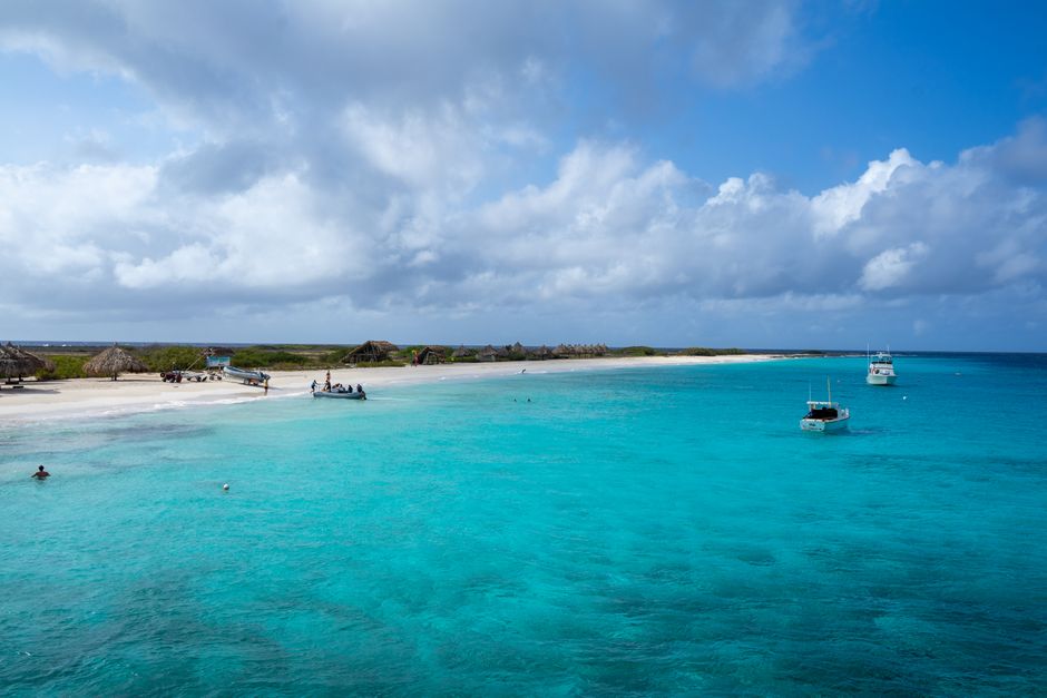 Experience the serene beauty of a Curaçao beach, with vibrant turquoise waters and scattered boats under a vast sky.