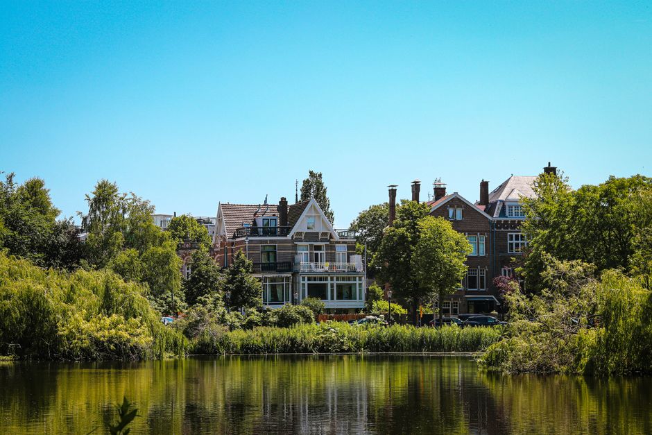Beautiful historic houses by the water in Amsterdam showcasing vibrant architecture and lush greenery.
