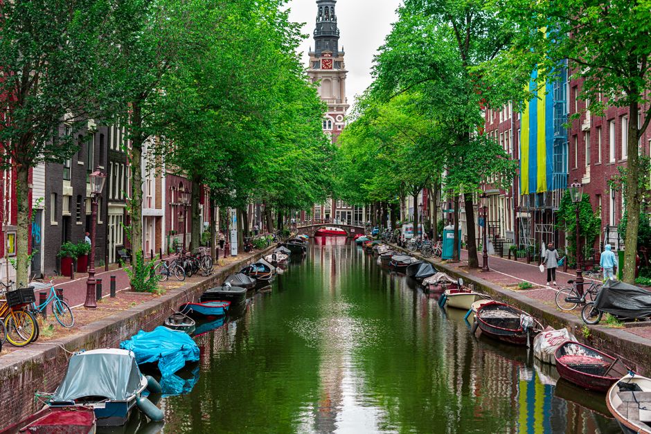 Peaceful Amsterdam canal with boats and view of Zuiderkerk tower.