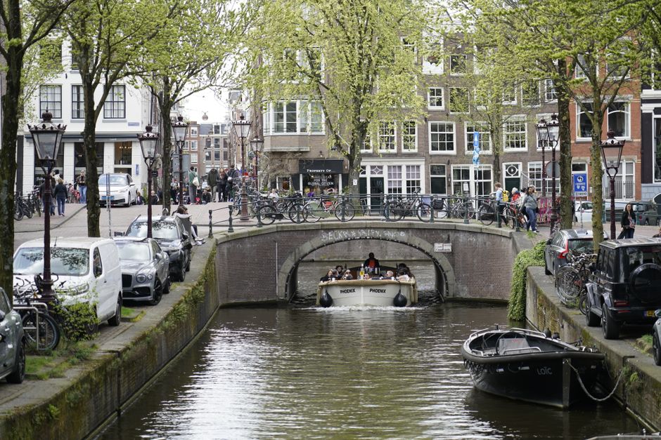 Charming scene of boats navigating a canal in Amsterdam, featuring classic architecture and a bustling street.