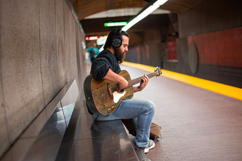 A street musician playing guitar and wearing headphones in a subway station, showcasing urban culture.