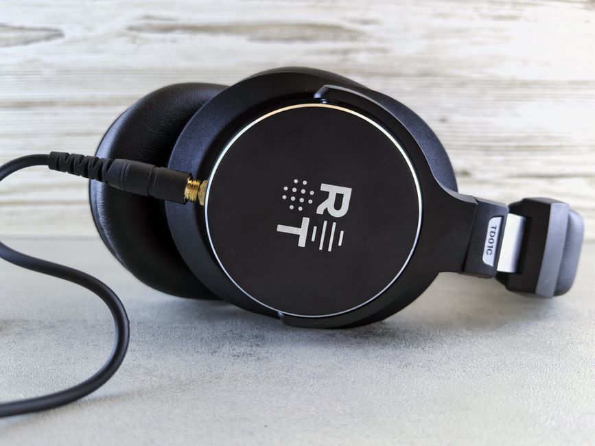 Close-up of black wired headphones with a visible logo on a wooden surface.