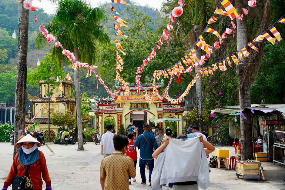 Vibrant temple courtyard decorated with colorful flags and people celebrating during the day.