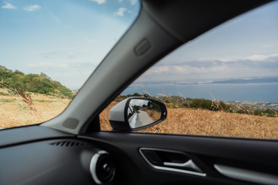 View of a coastal landscape through a car window, capturing the open road and distant horizon.