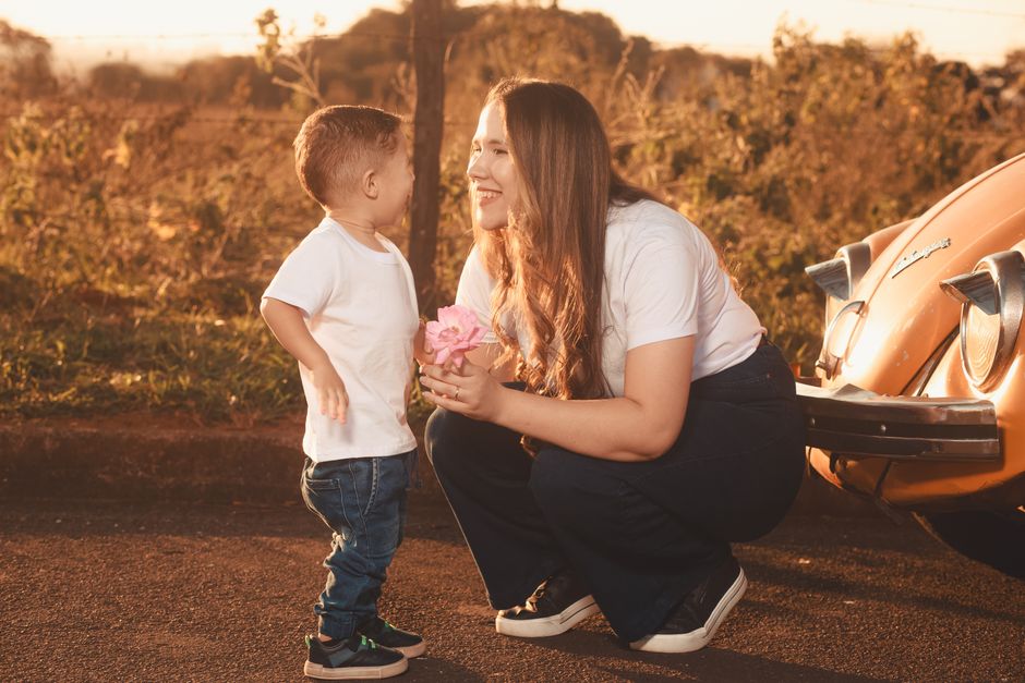 A joyful moment between a mother and child near a vintage car at sunset.