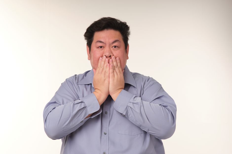 Portrait of a man covering his mouth with his hands, expressing surprise, against a neutral background.