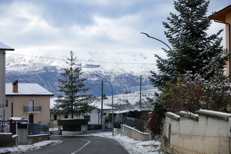 Scenic snow-covered village road with mountain backdrop under a cloudy winter sky.