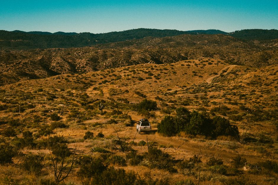White SUV driving off-road through desert landscape under clear blue sky.