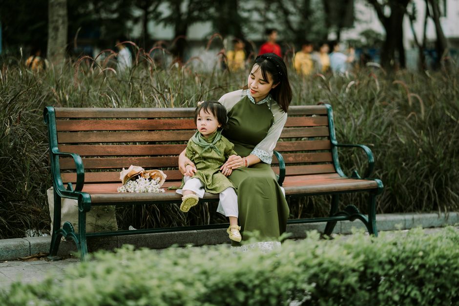 A mother and daughter in green traditional clothing sit on a park bench, showcasing bonding and love.