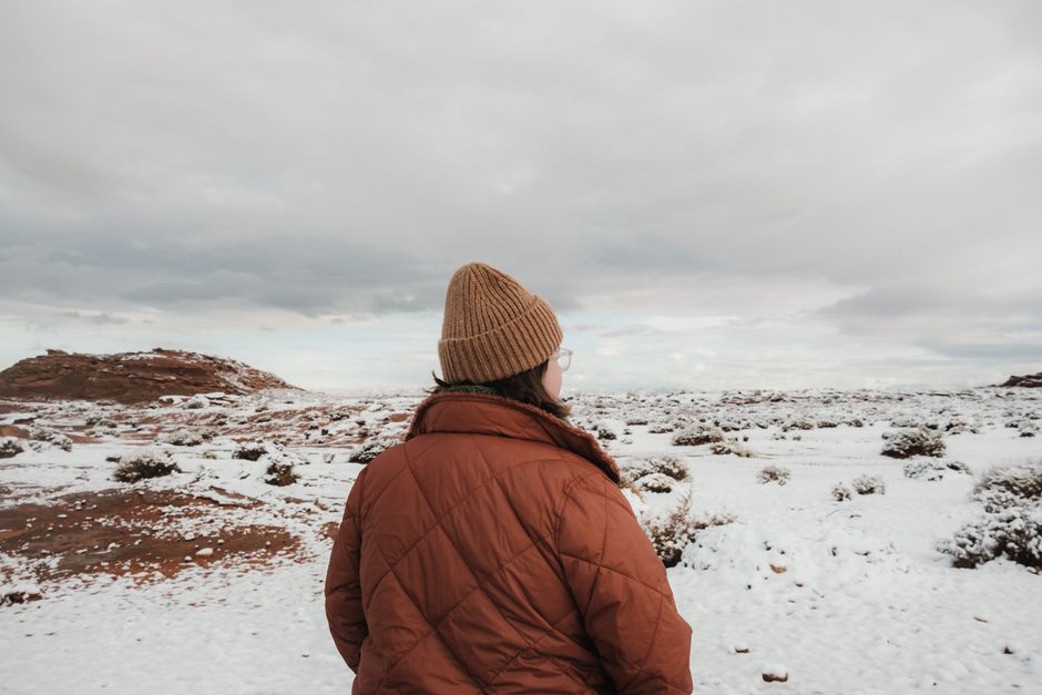 A person in winter attire exploring a snowy desert landscape under cloudy skies.