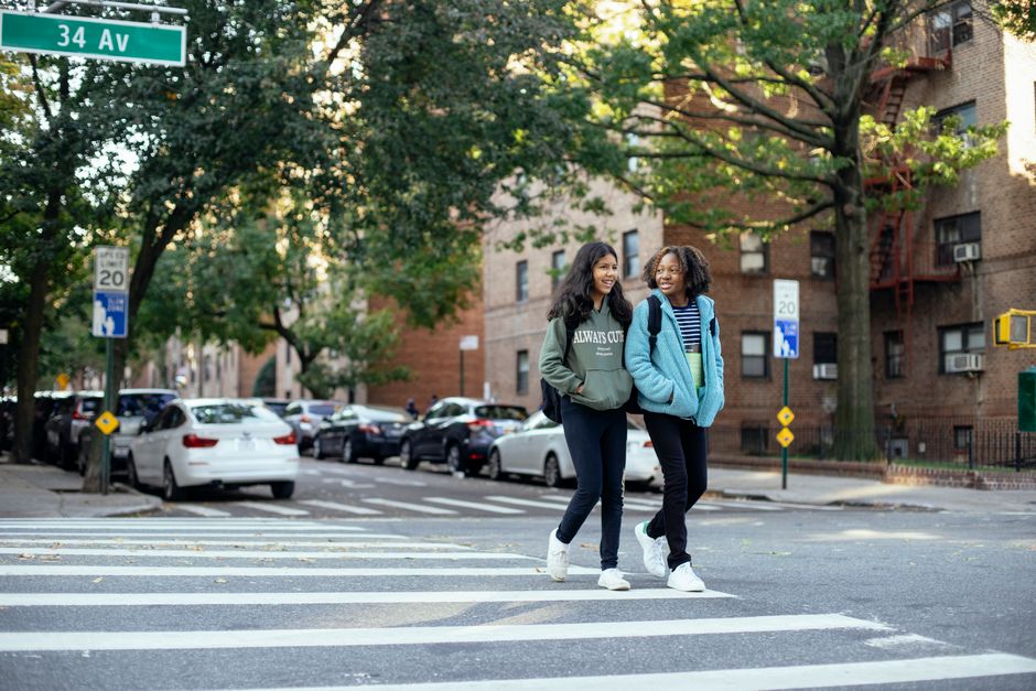 Full length of happy multiracial girlfriends in casual clothes crossing road while walking together in city
