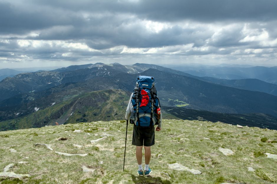Man with backpack hiking on Hoverla Mountain in Ukraine. Cloudy skies and scenic view create a sense of adventure.
