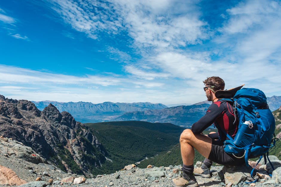 A man sits on rocky terrain, enjoying a scenic mountain view.