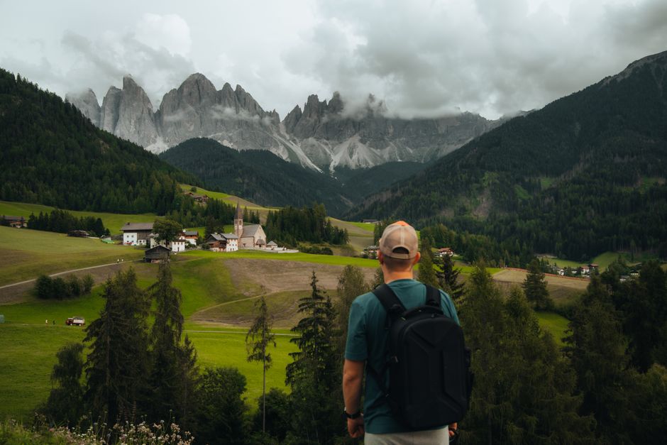 A hiker with a backpack overlooks a village nestled in the beautiful Dolomites mountains.