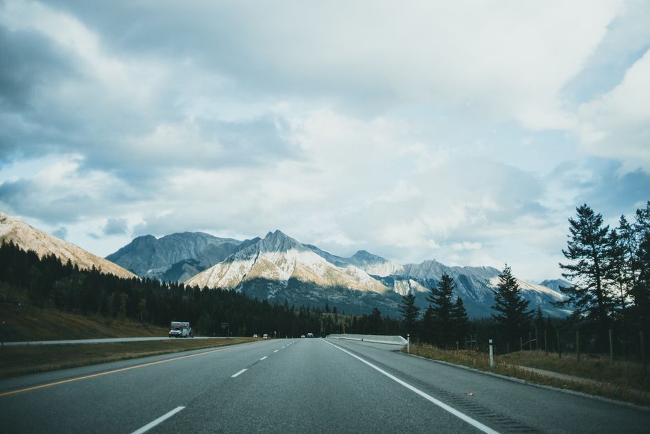 Open road stretching towards majestic mountain range under a cloudy sky.