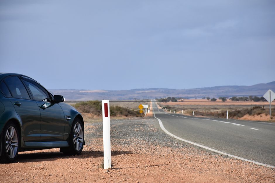 A parked car beside an open highway in a vast, serene landscape under a clear sky.