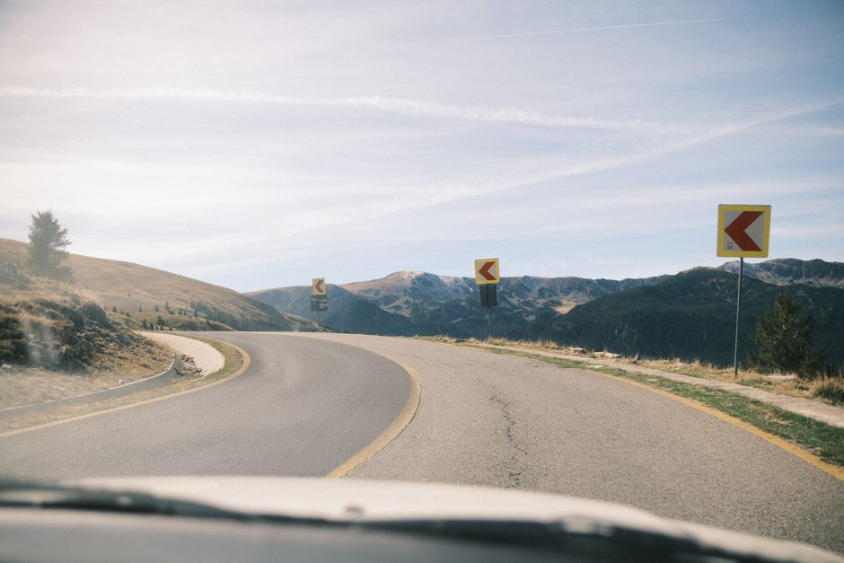 A curving road with traffic signs in a mountainous landscape during autumn, portraying calmness and adventure.