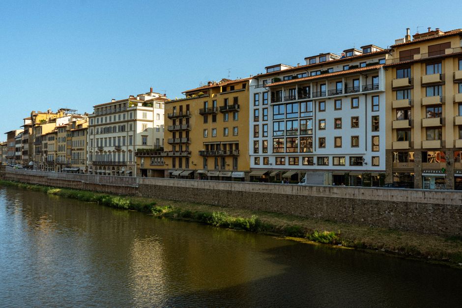 Charming riverside buildings in Florence, Italy, reflecting in the calm waters under a clear blue sky.