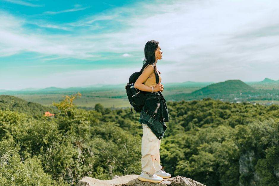 Asian woman backpacker on a cliff, enjoying a breathtaking forest view.