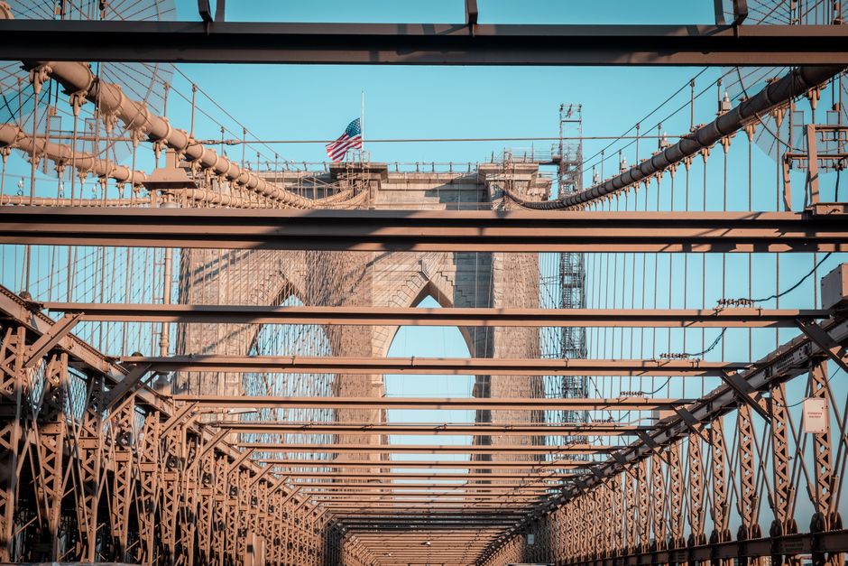 Iconic Brooklyn Bridge with American flag in clear daylight, showcasing its intricate architecture.