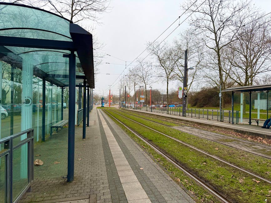 View of an empty tram stop in Müllheim, Germany, with visible tracks and glass shelters.