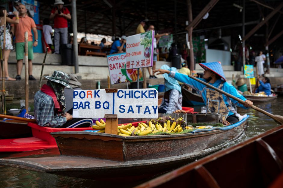 Vibrant scene of a floating market with a food stall selling satay and barbecue.