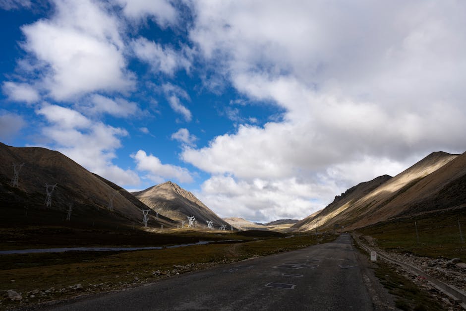 A picturesque mountain road with power lines under a bright blue sky with fluffy clouds.