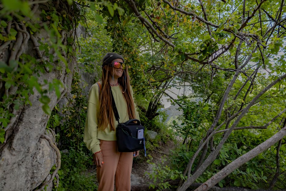 Woman in sunglasses and beanie smiles while exploring a lush green forest in spring. Perfect for adventure and travel themes.