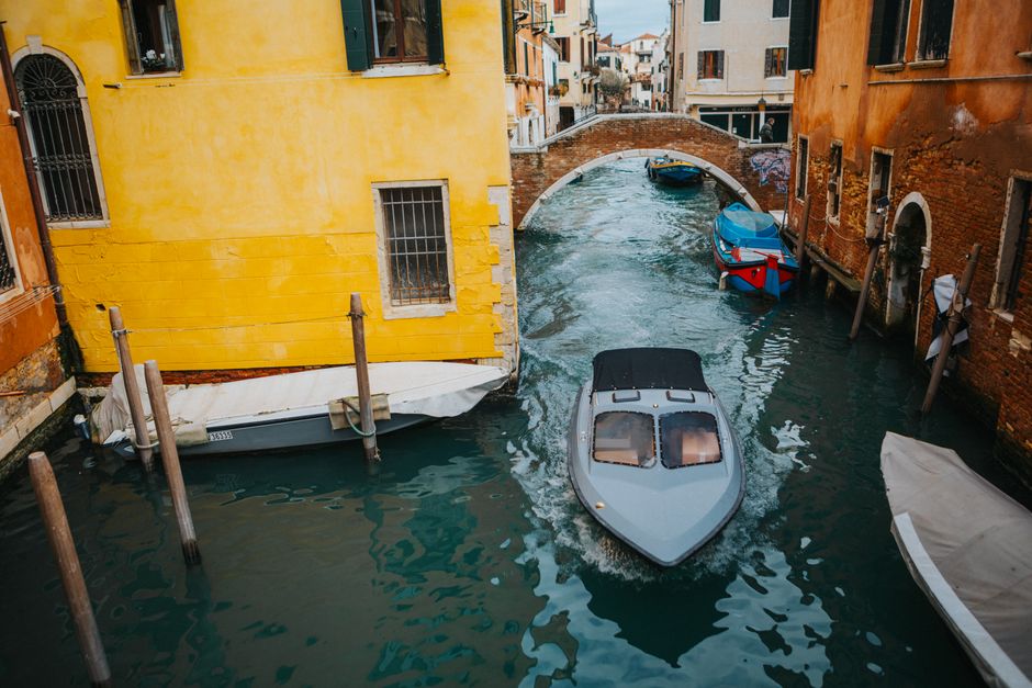 A sleek motorboat cruises through a picturesque Venetian canal, passing under a charming stone bridge.