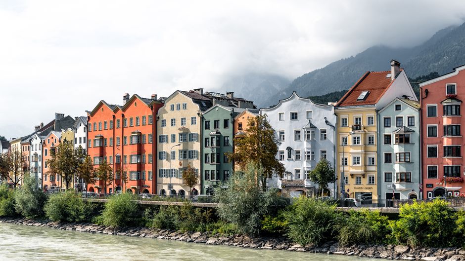 Vibrant facades along the river in Innsbruck, Austria, with alpine backdrop.
