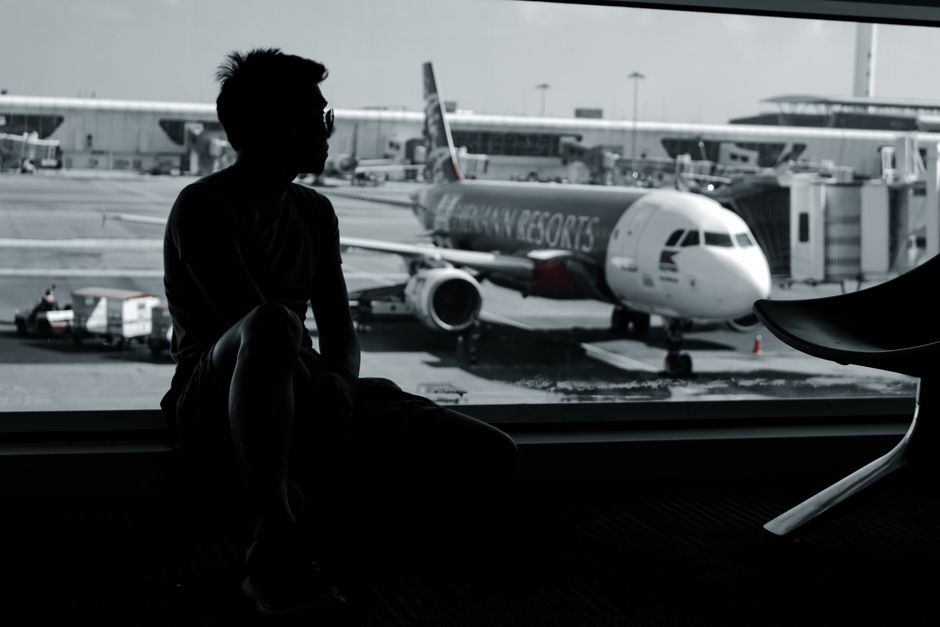 A silhouetted man sits in an airport terminal, viewing an airplane on the tarmac.