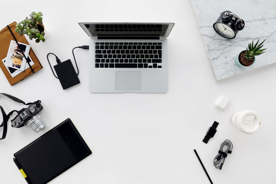 Top view of a minimalist workspace featuring a laptop, camera, and various electronic accessories on a white table.