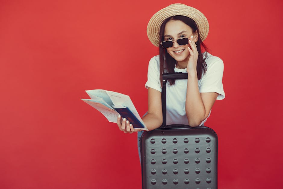 Delighted young woman in straw hat in casual clothes leaning on suitcase and checking tickets before traveling on red background
