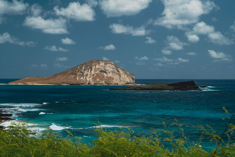 A breathtaking view of a rocky island surrounded by vivid blue ocean under a partly cloudy sky.