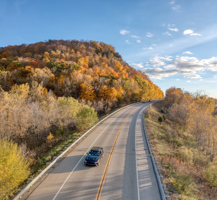 Aerial view of a car driving through vibrant autumn foliage on a country road in Stockholm, WI.